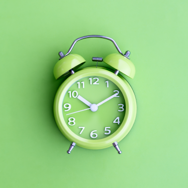 Green twin bell analog alarm clock against green background