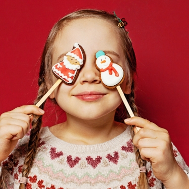 Little girl holding Holiday cookies over her eyes