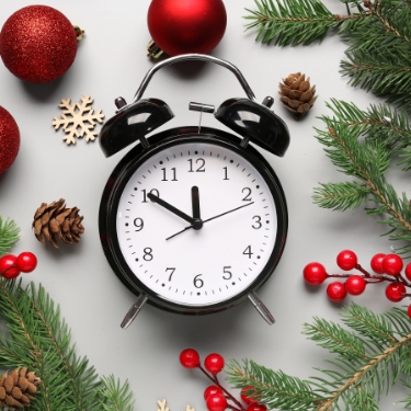 Black alarm clock with white face surrounded by holly and greenery