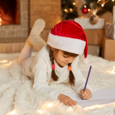 Little girl writing a letter to Santa while wearing a Santa hat